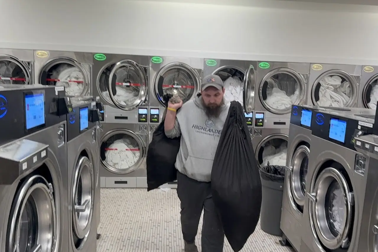 Highlander staff member carrying two bags of laundry past commercial washers in Nelsonville, Ohio